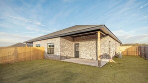Une maison de plain-pied avec une façade en briques, un porche à l’avant et une cour arrière clôturée.