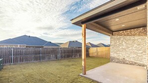 Une cour arrière clôturée avec un espace patio, une clôture en bois et un mur en briques.