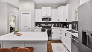 Une cuisine moderne avec des meubles blancs, des appareils en acier inoxydable et un îlot central.