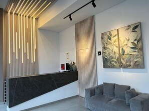 Ein moderner Empfangsbereich mit einem dunklen Empfangstresen, einem grauen Sofa und einem großen abstrakten Gemälde an der Wand.