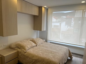 Ein Schlafzimmer mit Bett, Nachttischen und einem Fenster mit Blick auf Gebäude.