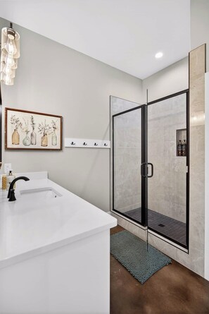 Une salle de bain moderne avec une douche à parois de verre, un lavabo blanc et une œuvre d’art florale encadrée accrochée au mur.