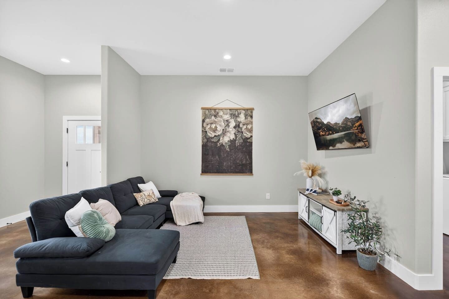A living room with a dark sofa, a white rug, and a painting on the wall.