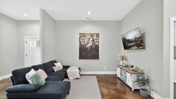 A living room with a dark sofa, a white rug, and a painting on the wall.