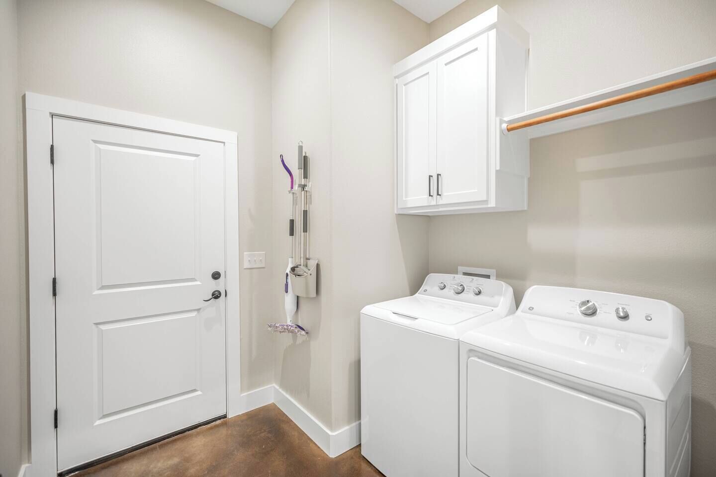 A laundry room with two white washing machines, a drying rack, and a door.
