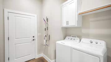 A laundry room with two white washing machines, a drying rack, and a door.