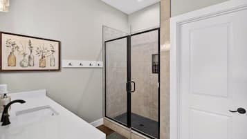 A bathroom with a white sink, a glass shower enclosure, and a door with a handle.