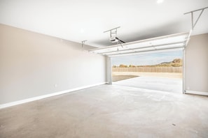 Un garaje con piso de concreto, puerta blanca y estructura de techo metálica.