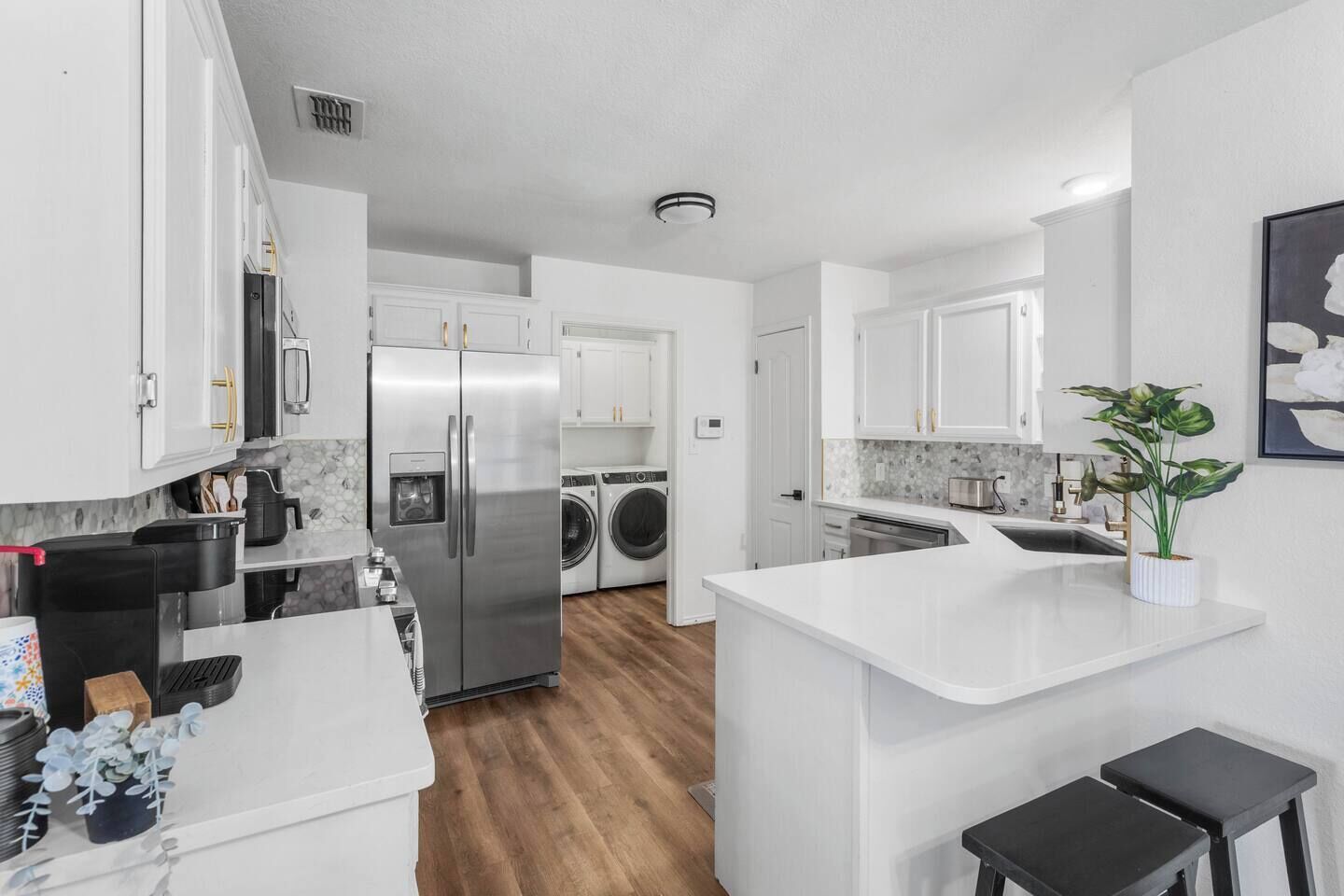A modern kitchen with white cabinetry, a stainless steel refrigerator, a built-in washing machine, and a small island with stools.