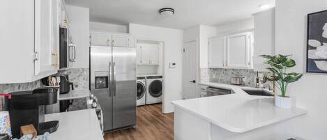 A modern kitchen with white cabinetry, a stainless steel refrigerator, a built-in washing machine, and a small island with stools.