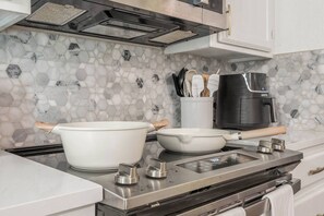 Eine Küche mit einem modernen Herd, einem großen weißen Topf, einer kleineren weißen Schüssel und einer Kaffeemaschine.