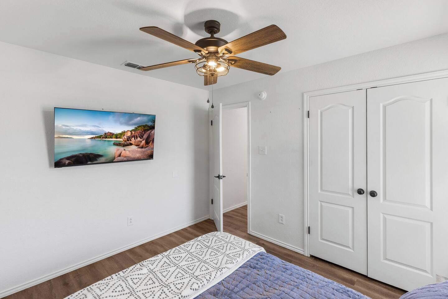Una habitación con ventilador de techo, un cuadro enmarcado, una puerta blanca y un tapete estampado.