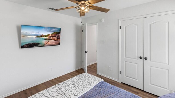 Une pièce avec un ventilateur de plafond, un tableau encadré, une porte blanche et un tapis à motifs.