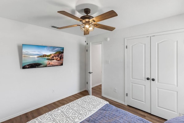 Une pièce avec un ventilateur de plafond, un tableau encadré, une porte blanche et un tapis à motifs.
