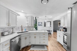 A modern kitchen with white cabinetry, a built-in dishwasher, and a central island. - Stylish 3BR+2 Bath Home w/Big Yard! (Abilene)