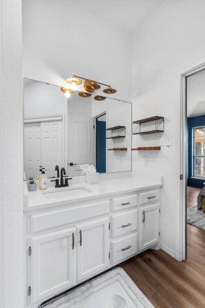 Une salle de bain avec un meuble-lavabo blanc, un grand miroir, un luminaire doré et un mur d’accent bleu.