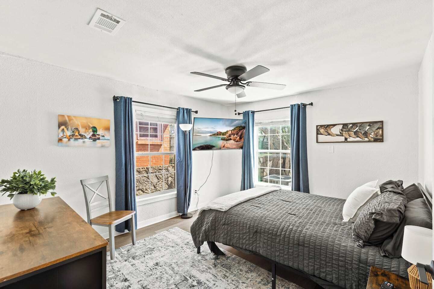 Quarto com cama, escrivaninha, cadeira, planta em vaso e janela com cortinas.