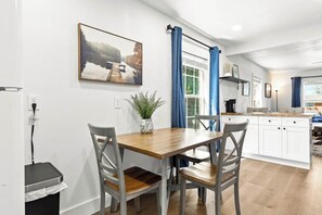 A dining area with a wooden table and chairs, a potted plant, and a painting of a lake.