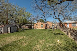 A residential property with a grassy yard, a shed, and a brick house with a porch.