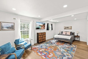 A bedroom with a bed, a dresser, a chair, a rug, and artwork on the walls.