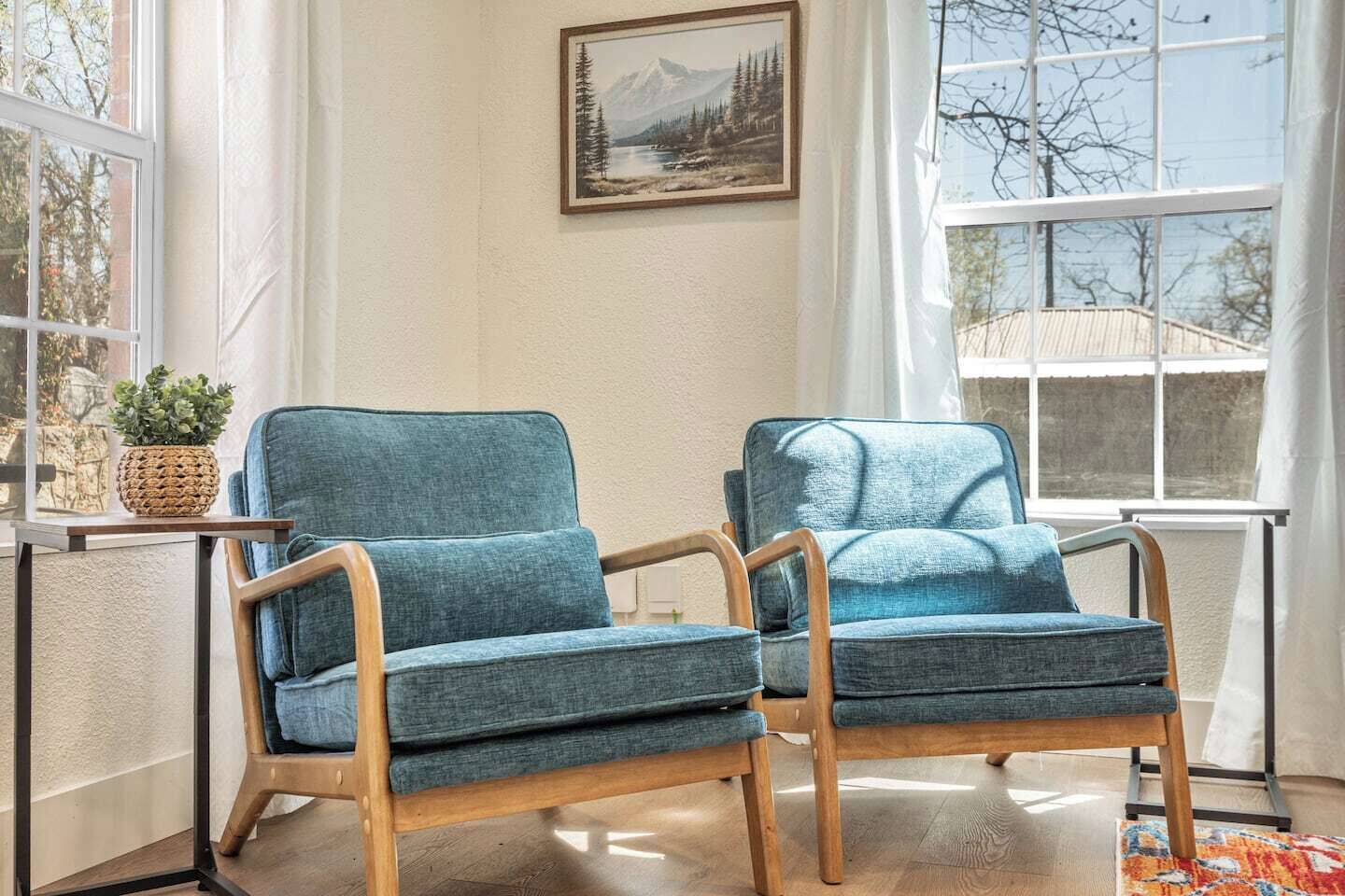 Dos sillones tapizados en azul con armazones de madera, una maceta tejida y un cuadro de paisaje enmarcado en una pared.