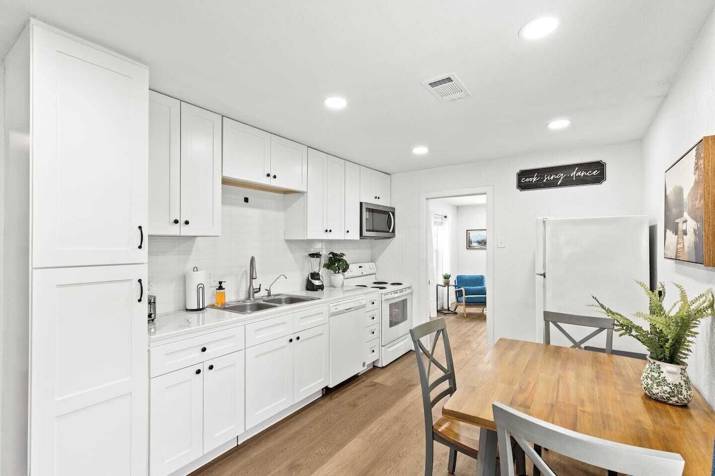 Una cocina moderna con armarios blancos, una mesa de comedor de madera y un microondas.
