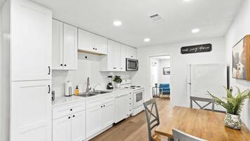 Una cocina moderna con armarios blancos, una mesa de comedor de madera y un microondas.