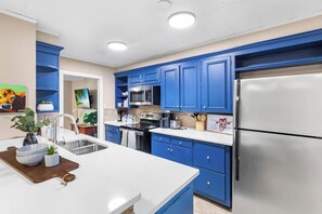 A modern kitchen with blue cabinets, stainless steel appliances, and a white countertop. - Modern Comfort 4BR House w/ Large Yard (Abilene)