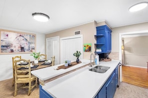 A kitchen with a central island, white countertops, blue cabinets, and a dining area with wooden chairs and a table. - Modern Comfort 4BR House w/ Large Yard (Abilene)