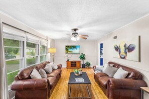 A living room with leather sofas, a coffee table, a ceiling fan, and artwork on the walls. - Modern Comfort 4BR House w/ Large Yard (Abilene)