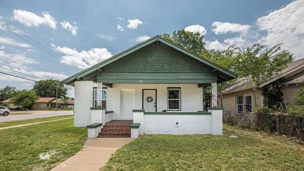A single-story house with a green roof, white exterior walls, and a front porch with steps leading to the door. - Modern 2BR Home with Pool Table & Yard (Abilene)