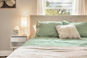 Une chambre à coucher avec un lit, une table de chevet avec une lampe et une fenêtre donnant sur des arbres.