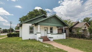 A single-story house with a green roof, white exterior walls, and a front porch with steps leading to the door. - Modern 2BR Home with Pool Table & Yard (Abilene)