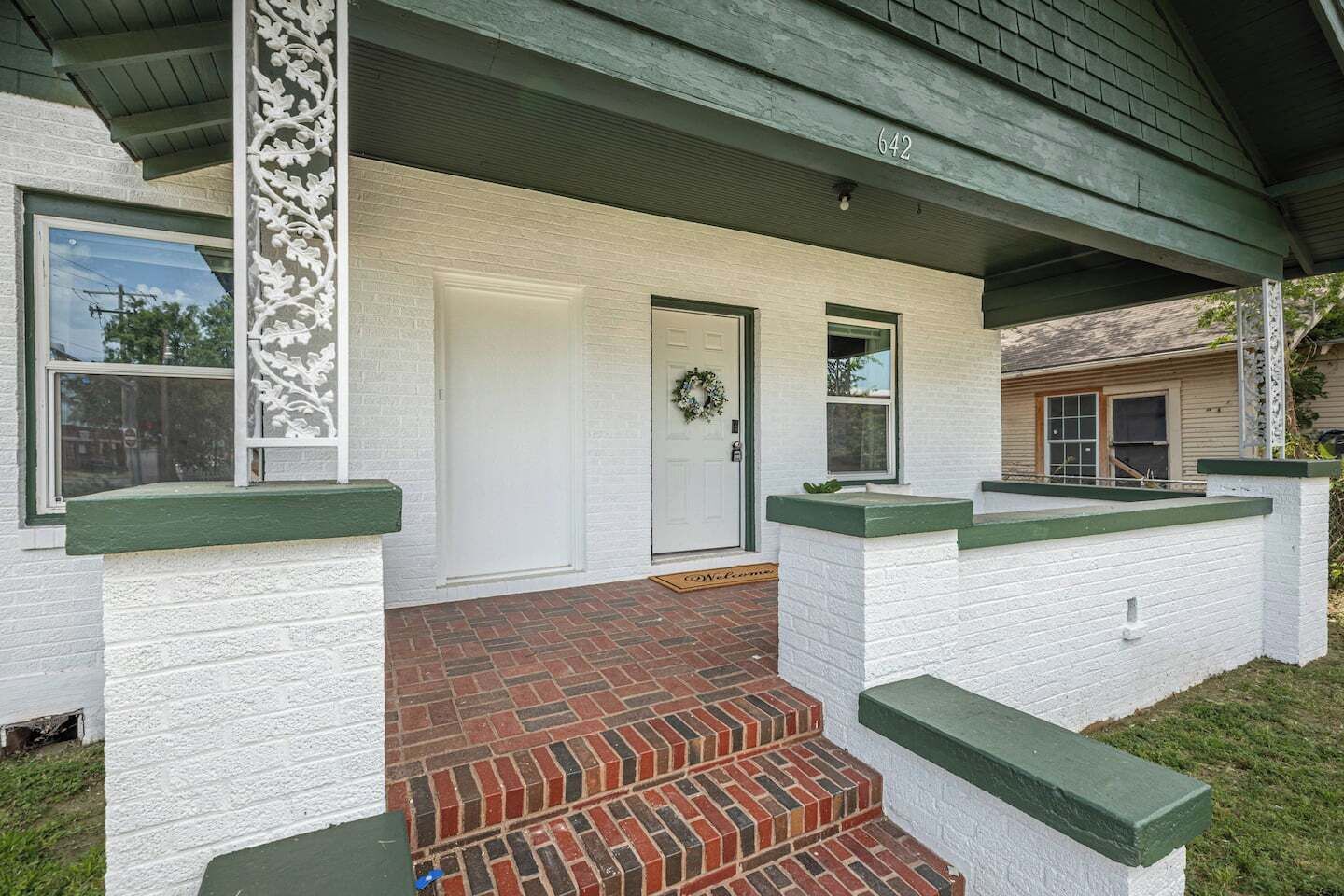 Ein Haus mit einer Ziegelfront, weißen Außenwänden und einem grünen Dach.