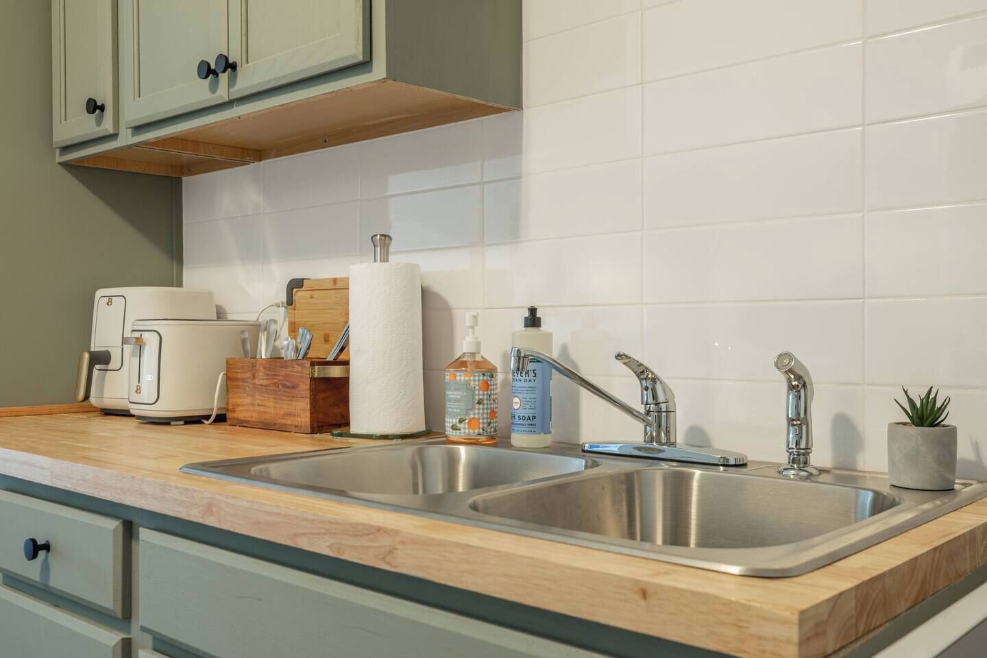Een keuken met een dubbele spoelbak, een broodrooster, een houten snijplank en een kleine potplant.