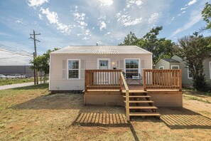 Une maison de plain-pied avec une terrasse à l’avant et un escalier menant à un balcon situé à l’étage.