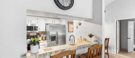 Una cocina moderna con armarios blancos, electrodomésticos de acero inoxidable, una barra de madera y dos sillas de madera.