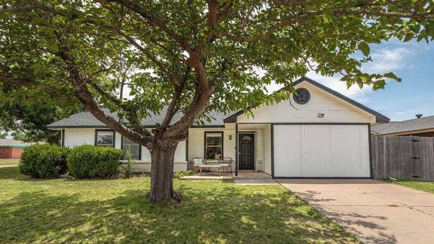 Uma casa térrea com garagem, varanda frontal e uma árvore no jardim.
