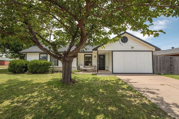Eingeschossiges Haus mit Garage, einer Veranda und einem Baum im Vorgarten.