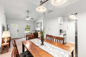 Ein Essbereich mit Holztisch, Stühlen, einer Pflanzvase, einem Deckenventilator und Pendelleuchten.