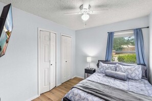 Une chambre à coucher avec un lit, une table de chevet, un ventilateur de plafond et une fenêtre avec des rideaux.