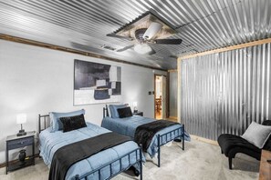 Ein Schlafzimmer mit zwei Betten, einem Deckenventilator, einem großen abstrakten Gemälde und Blick in einen anderen Raum.