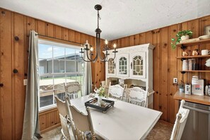 Une cuisine avec des lambris en bois, un lustre, des meubles de cuisine blancs et une table à manger avec des chaises.