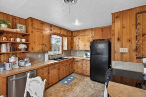 A kitchen with wooden cabinets, a black refrigerator, and a window. - Country Living: 3BR Hot Tub Escape: Close to all! (Abilene)