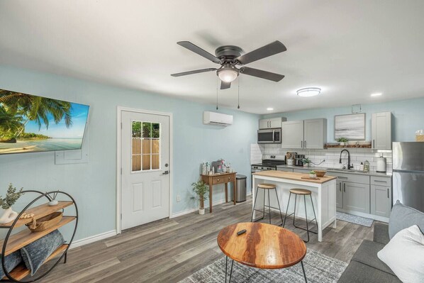 Una cucina moderna con isola centrale, ventilatore a soffitto e vista sulla spiaggia tramite una porta.