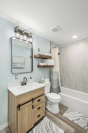 Un bagno con un mobile bagno in legno, un WC bianco, una vasca e una tenda da doccia.