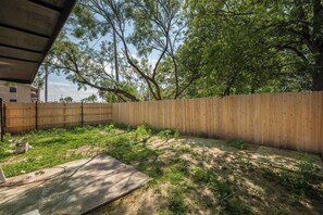 Een achtertuin met houten omheining, bomen en een terras van beton.