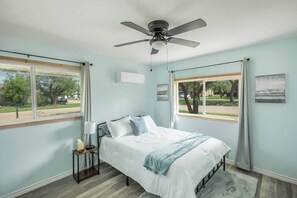 Una camera da letto con un letto, un comodino, una ventola a soffitto e due finestre.