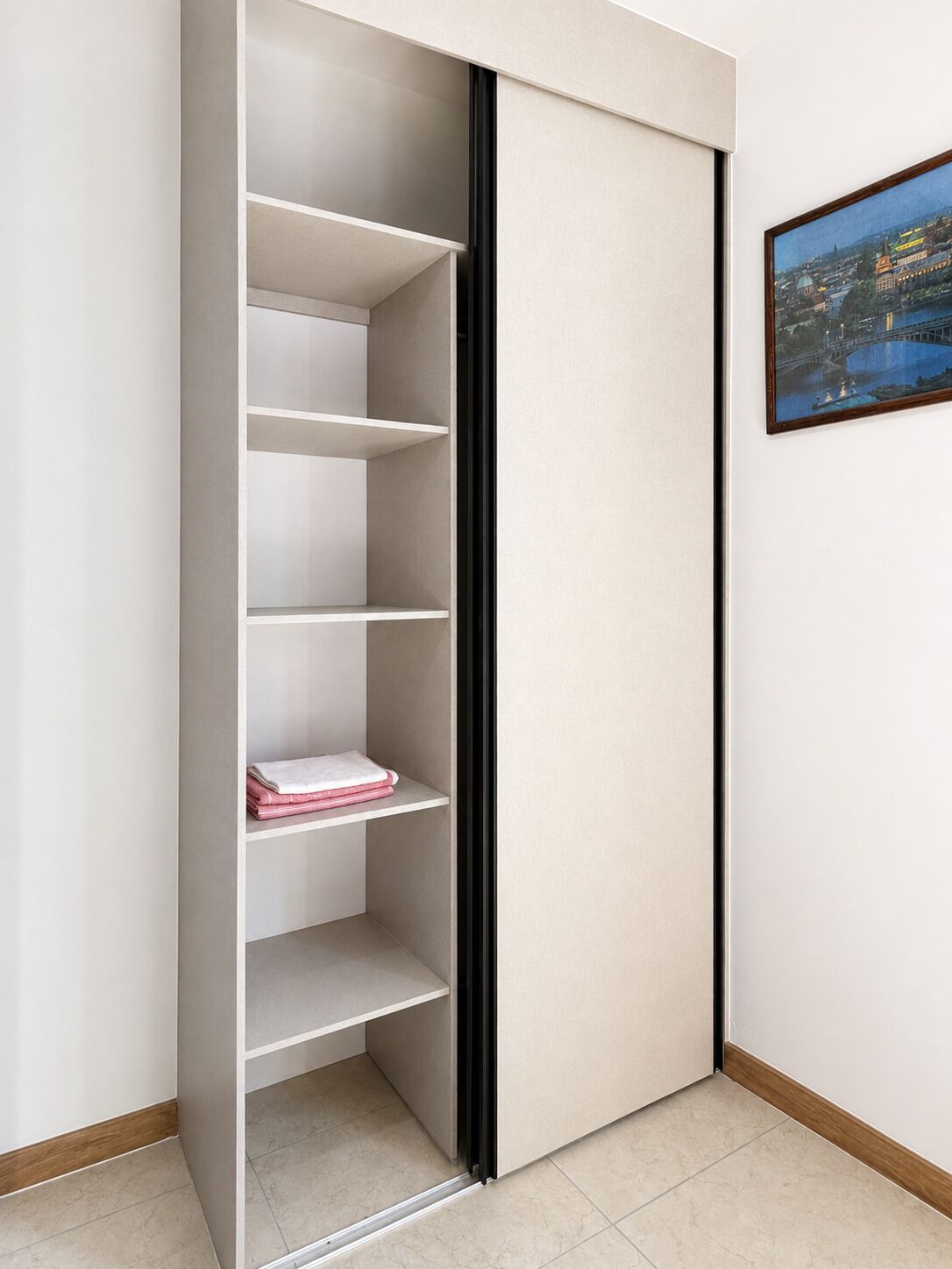 A closet with multiple shelves, a sliding door, and a framed picture on the wall.
