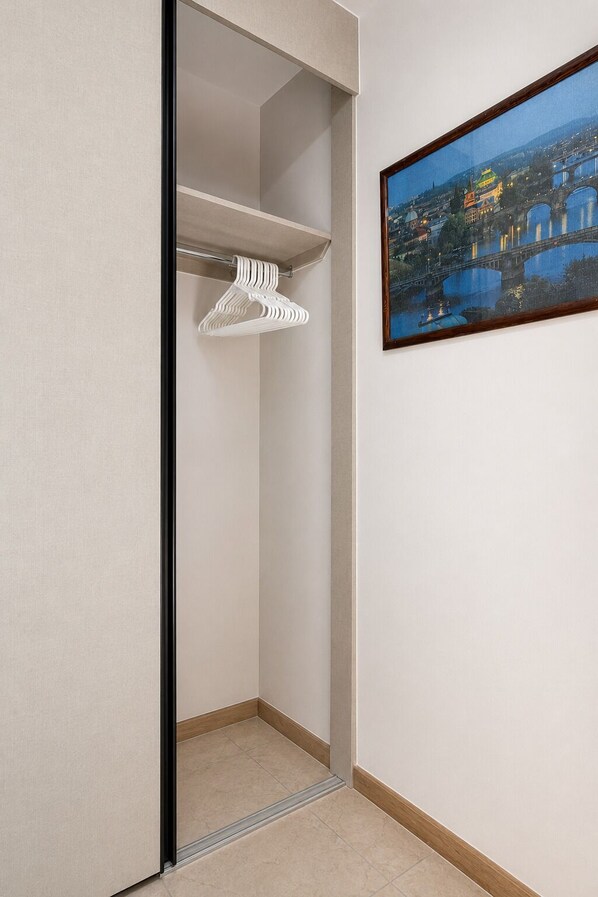 Een inloopkast met een kledingroede en een stadsgezichtschilderij in een lijst aan de muur.